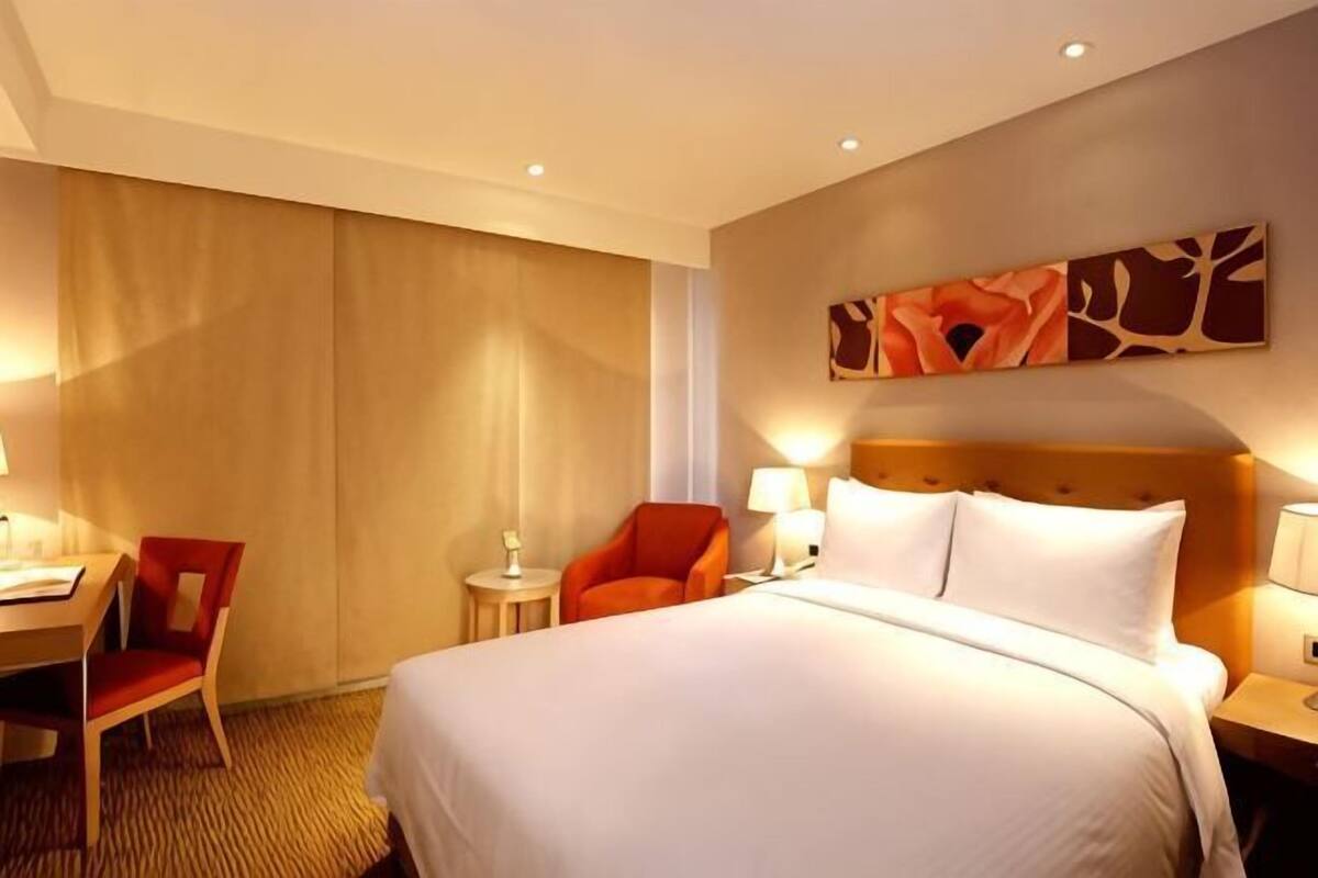 A hotel room with a bed, a desk, a chair, and a wall-mounted artwork.