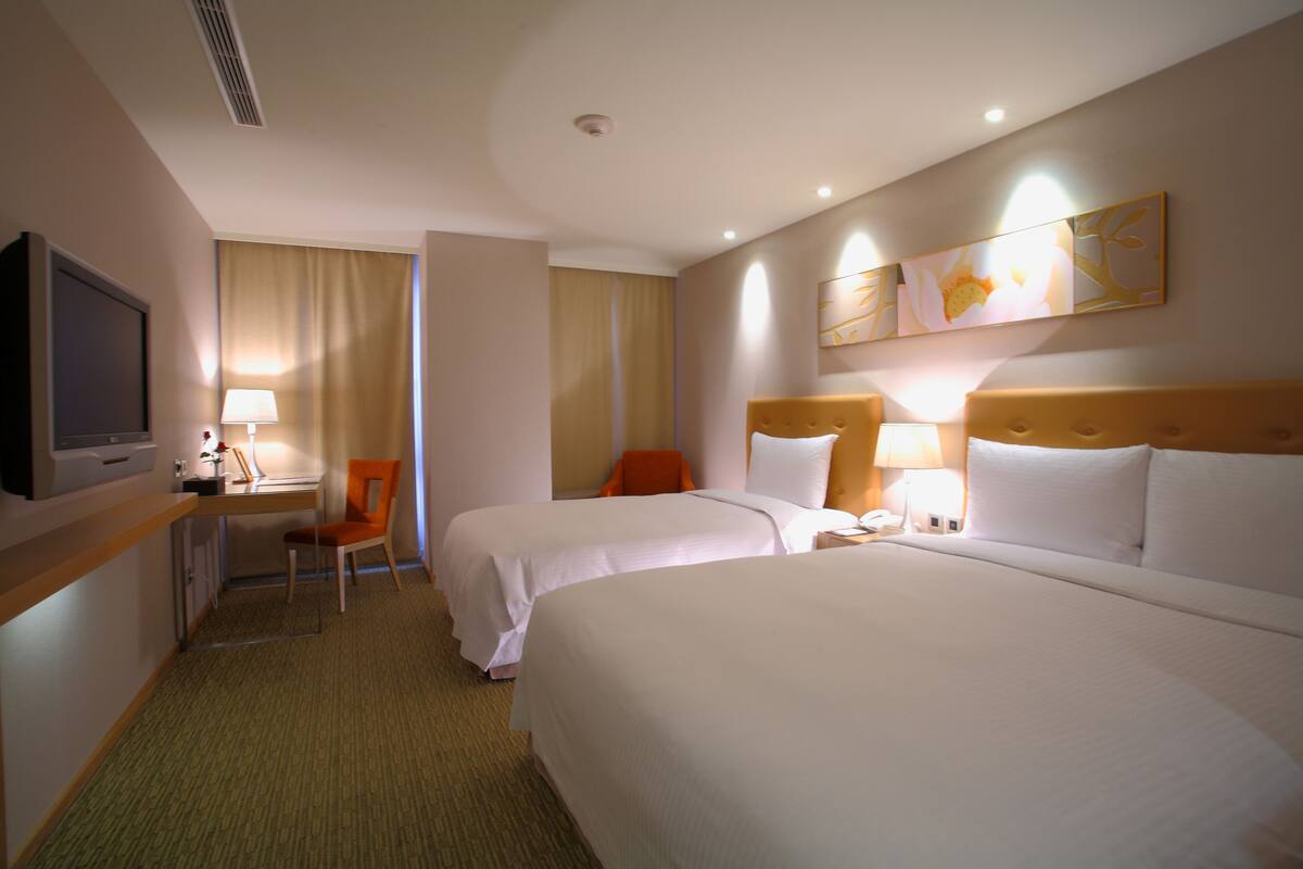 A hotel room with two beds, a desk with a chair, a television, and a painting on the wall.