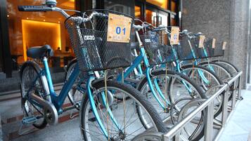 A row of blue bicycles with numbered rental tags, parked in front of a building with a glass facade.