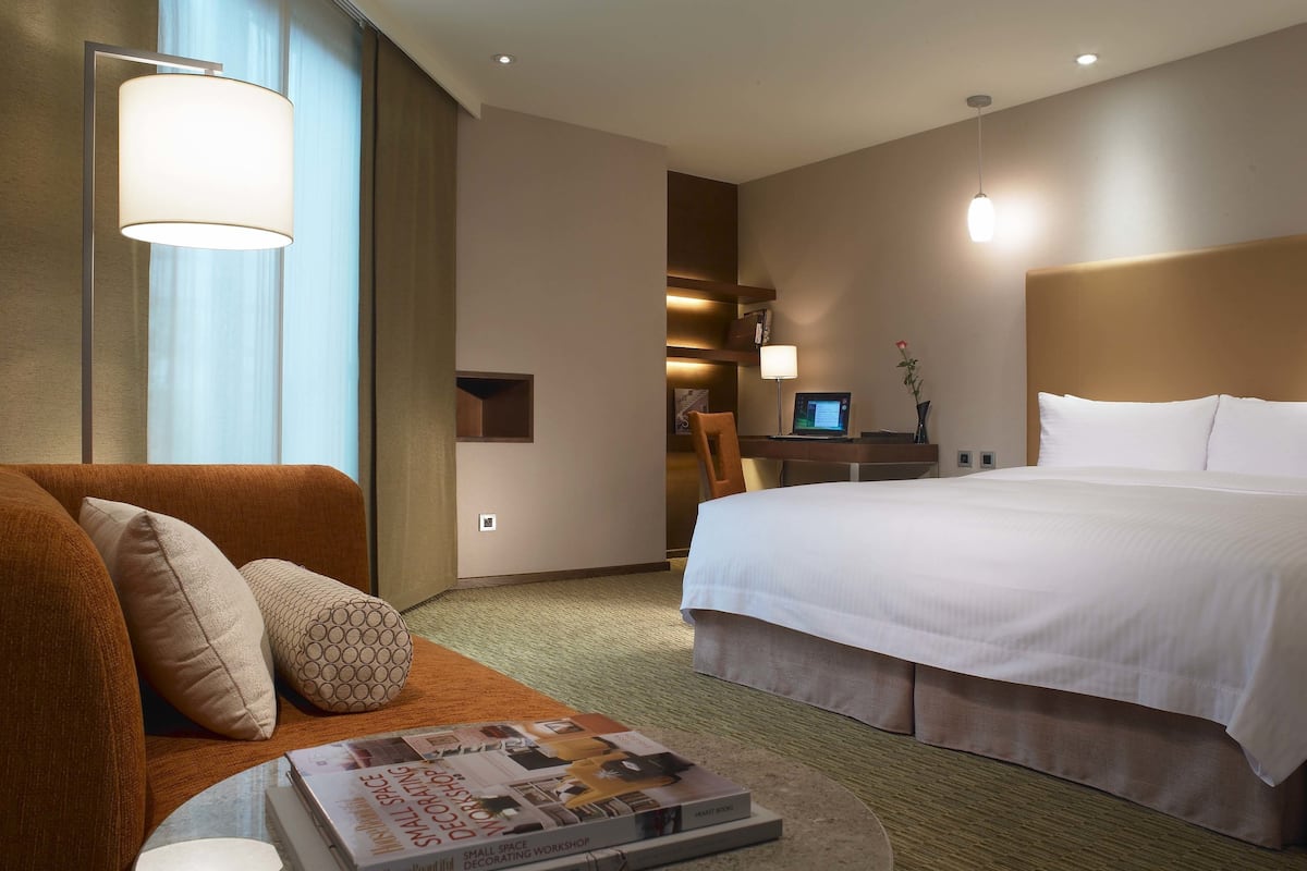 A hotel room with a large bed, a sofa, a desk with a laptop, and a magazine on a side table.