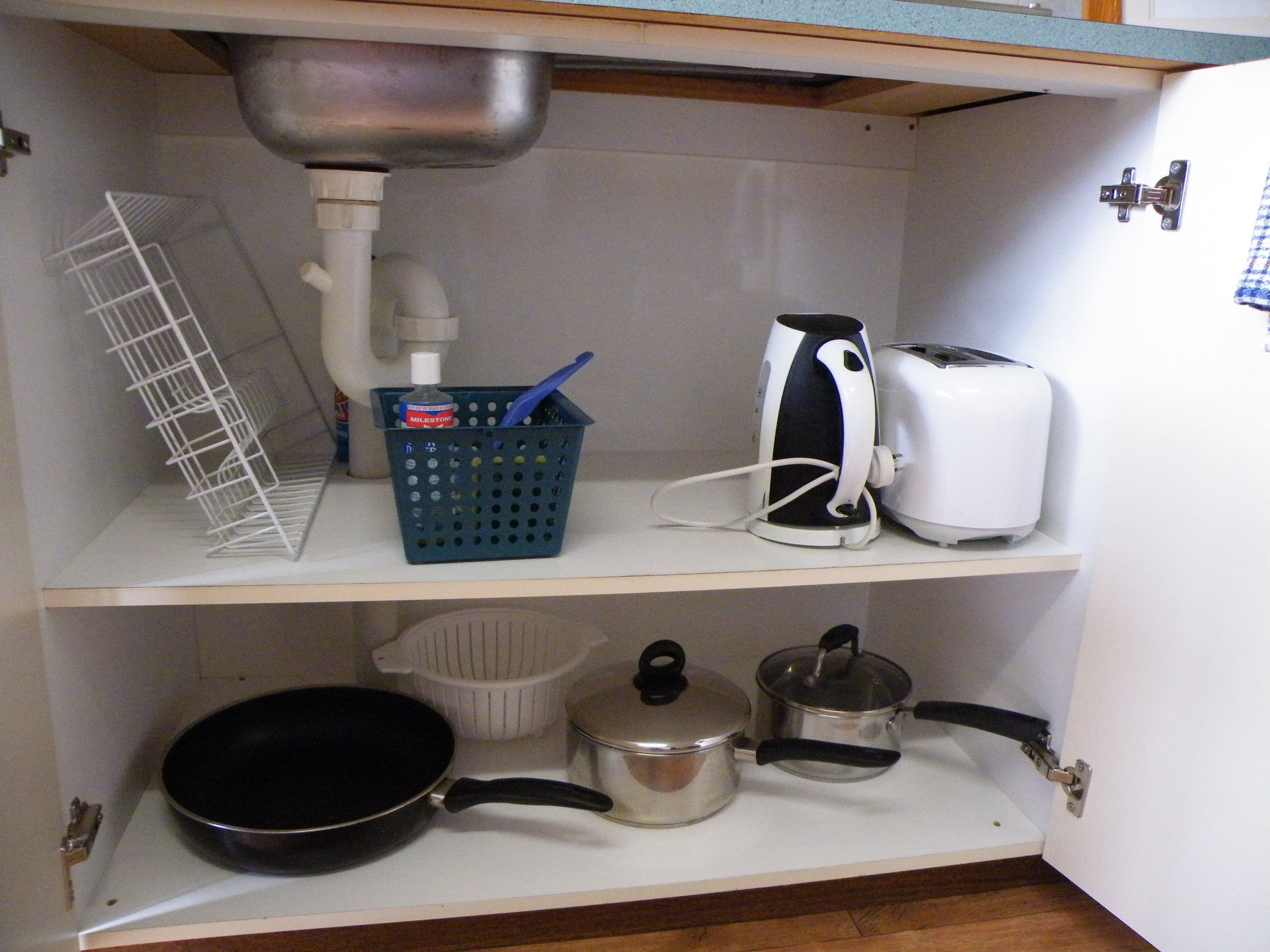 A kitchen with a sink, a toaster, a kettle, a frying pan, and a pot on the countertop.