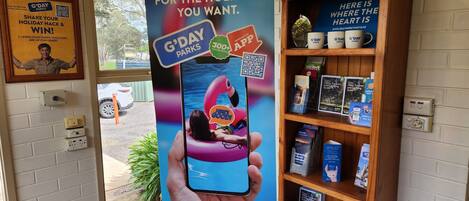 A promotional display for G'DAY Parks featuring a QR code, a G'DAY Parks app advertisement, and a shelf with camping-related items.