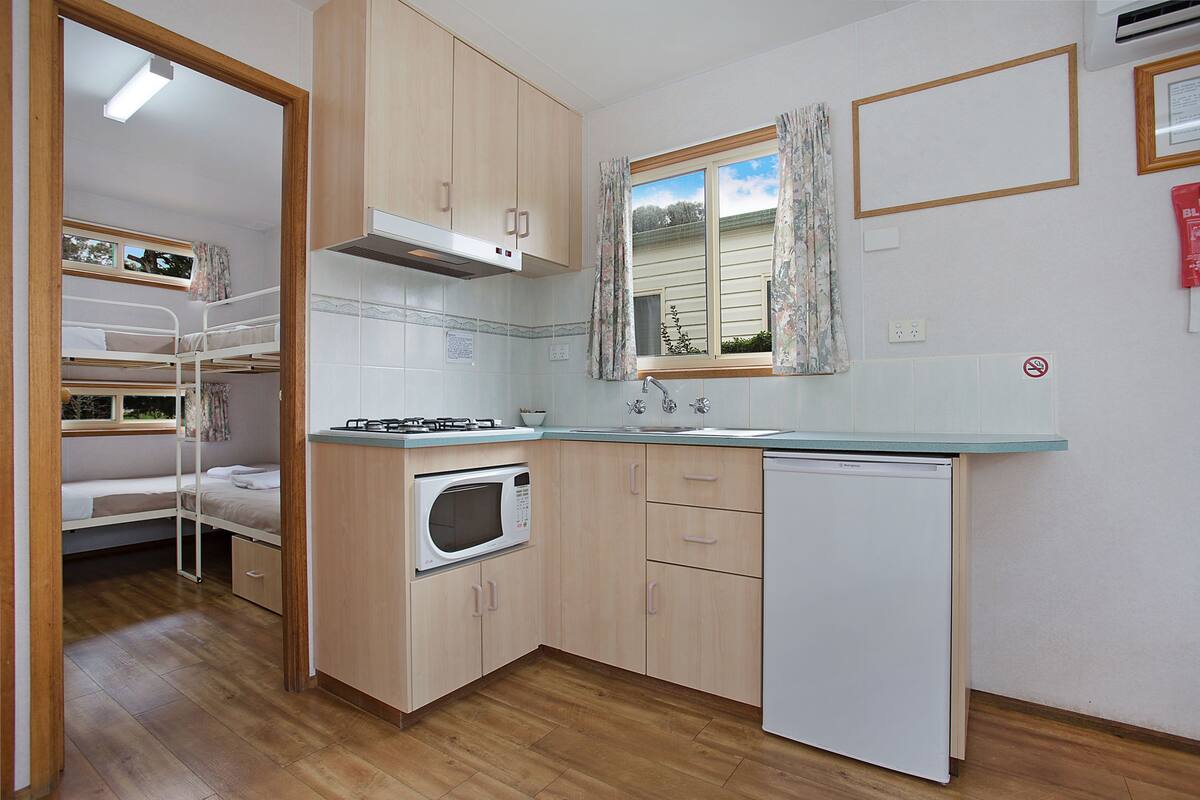 Eine kleine Küche mit Holzausstattung, einer Mikrowelle, einem Spülbecken und einem kleinen Kühlschrank.