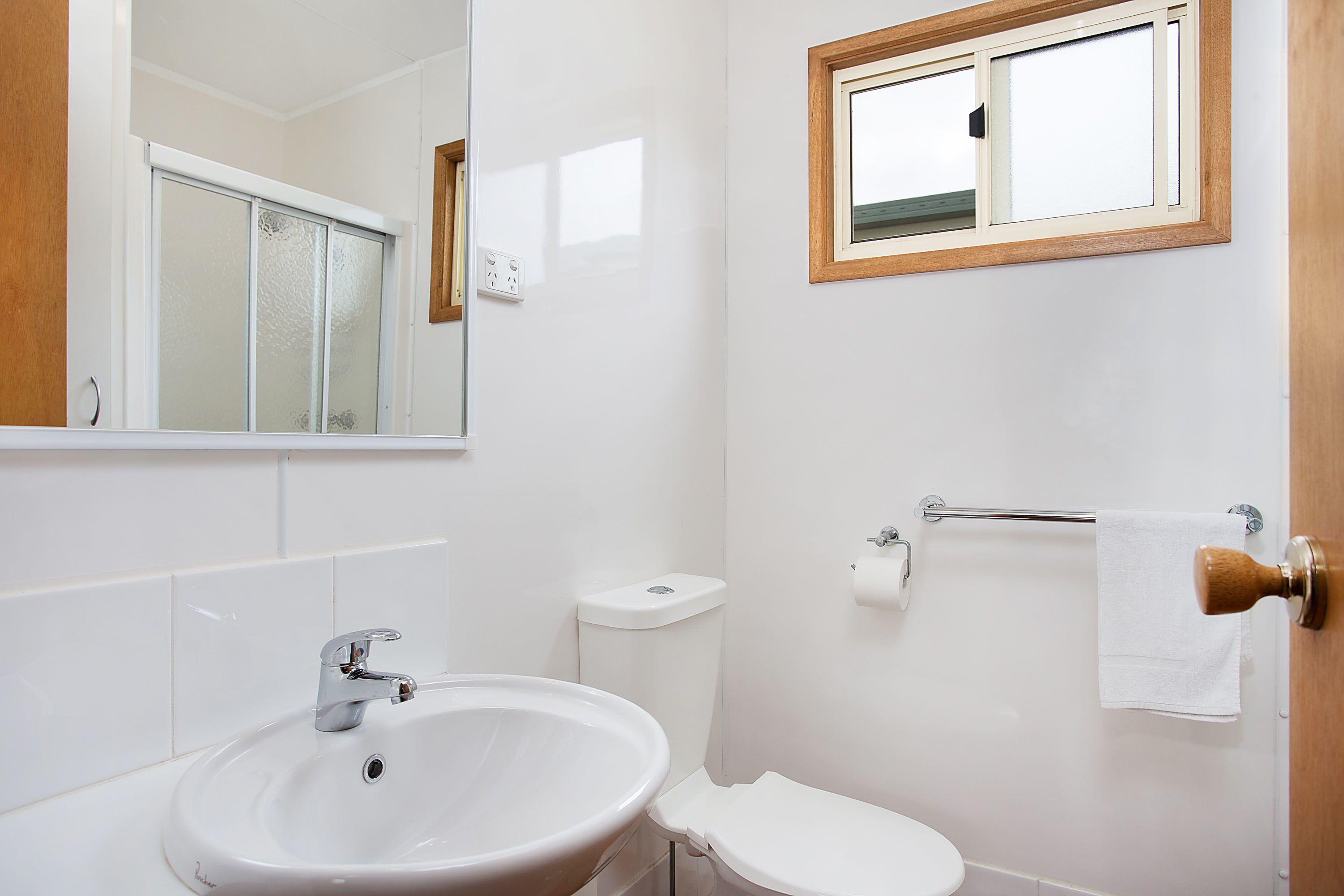 Un baño con lavamanos blanco, inodoro y una ventana sobre el inodoro.