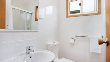 Un baño con lavamanos blanco, inodoro y una ventana sobre el inodoro.