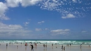A beach with people walking and surfing, and a clear sky. - Bluebottle Guest House (Cape Town)