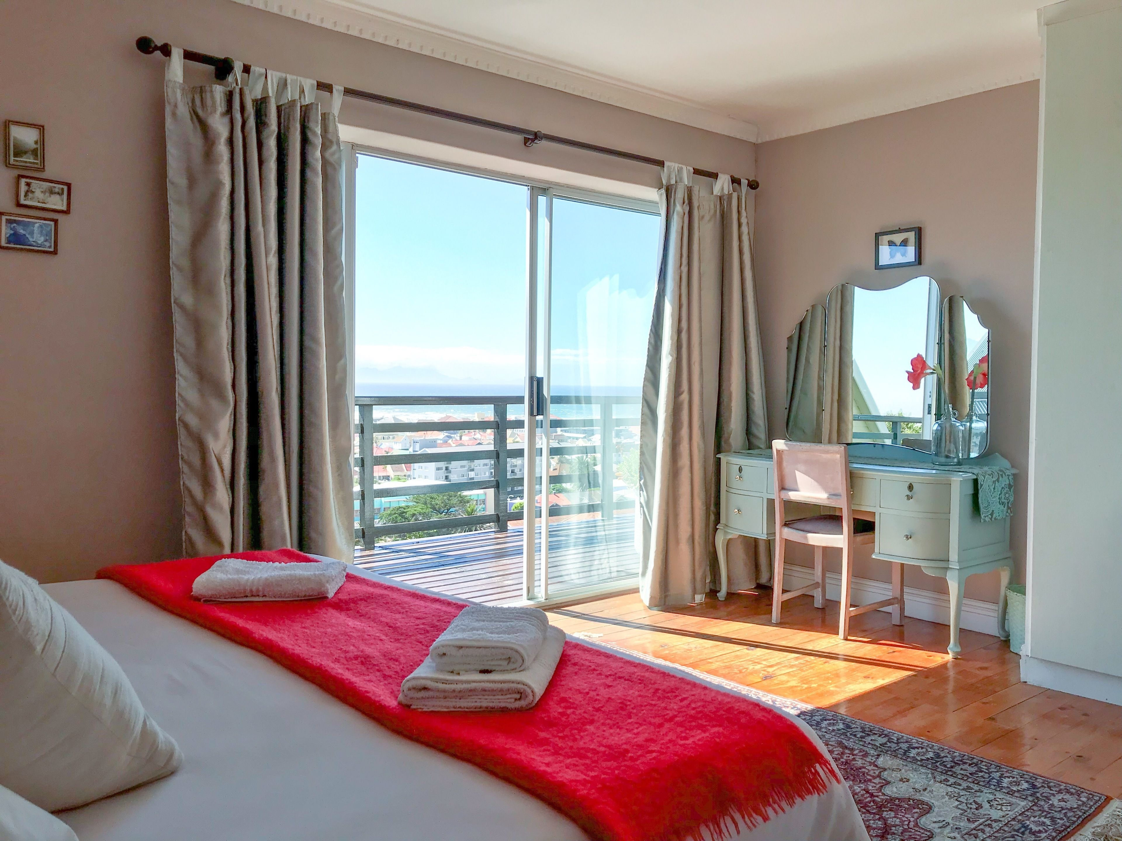 A bedroom with a bed, a desk, a chair, a dresser, and a large window with curtains.