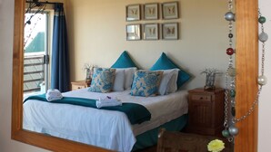 A neatly made bed with blue and white bedding, a wooden nightstand with a lamp, and a mirror reflecting the room. - Bluebottle Guest House (Cape Town)