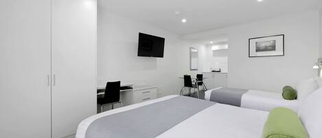 A modern hotel room with a large bed, a desk, a chair, and a flat-screen TV mounted on the wall.