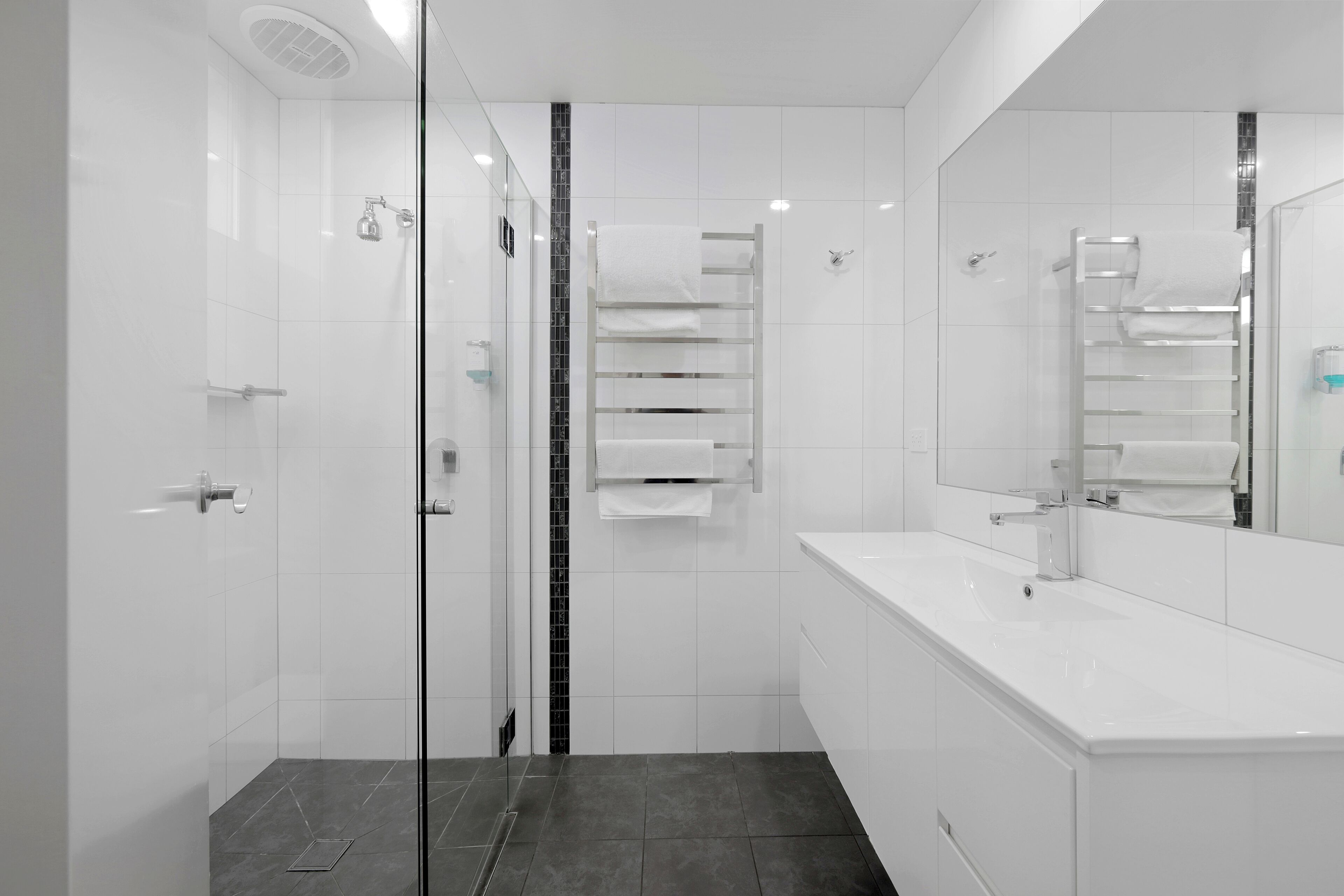 A modern bathroom with a glass shower enclosure, a white vanity with a mirror, and a towel rack.