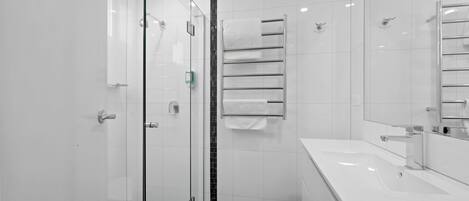 A modern bathroom with a glass shower enclosure, a black-tiled floor, a white sink with a mirror, and a towel rack with two towels.