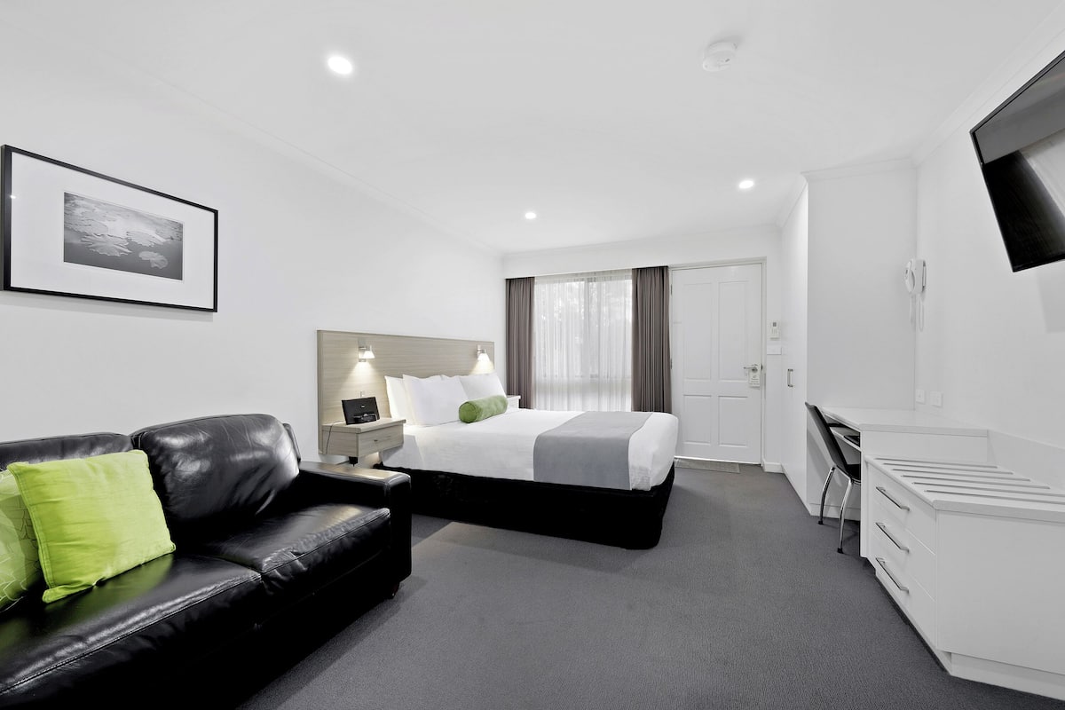 Une chambre d’hôtel moderne équipée d’un lit, d’un canapé en cuir noir, d’un bureau et d’un téléviseur à écran plat.
