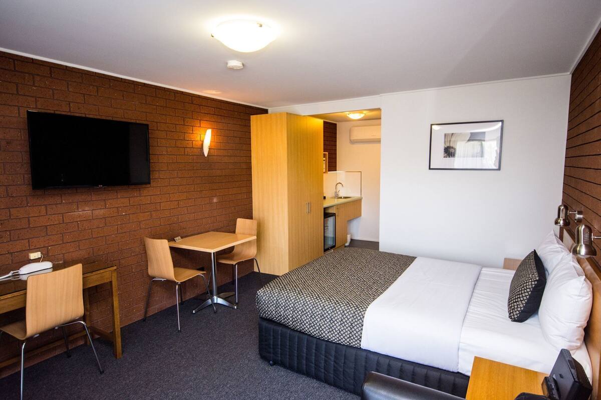 Une chambre d’hôtel équipée d’un lit, d’un bureau, d’une chaise, d’une télévision, d’une petite kitchenette et d’une salle de bain.