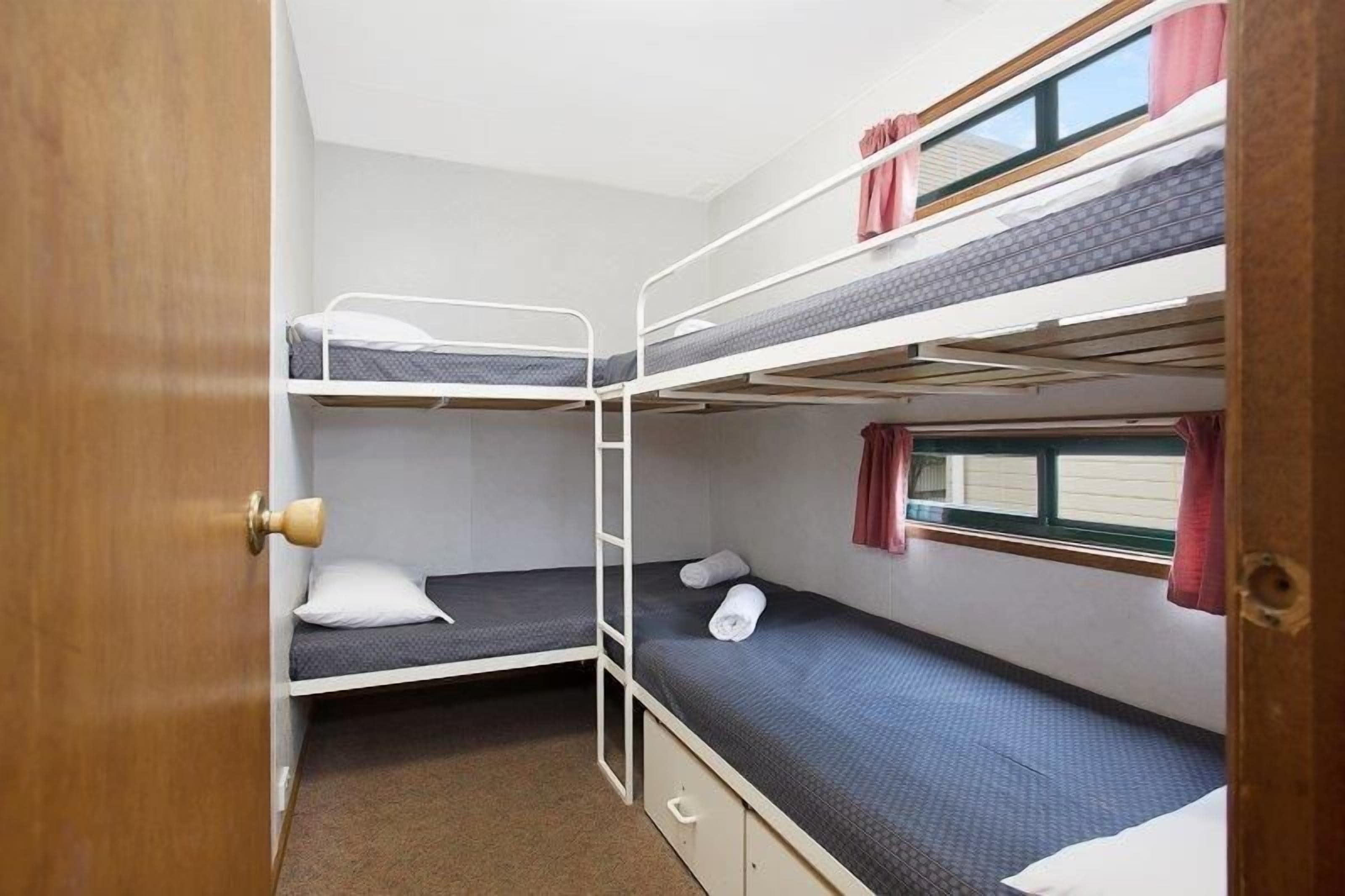 A bunk bed room with a wooden door, a ladder, and a window with curtains.