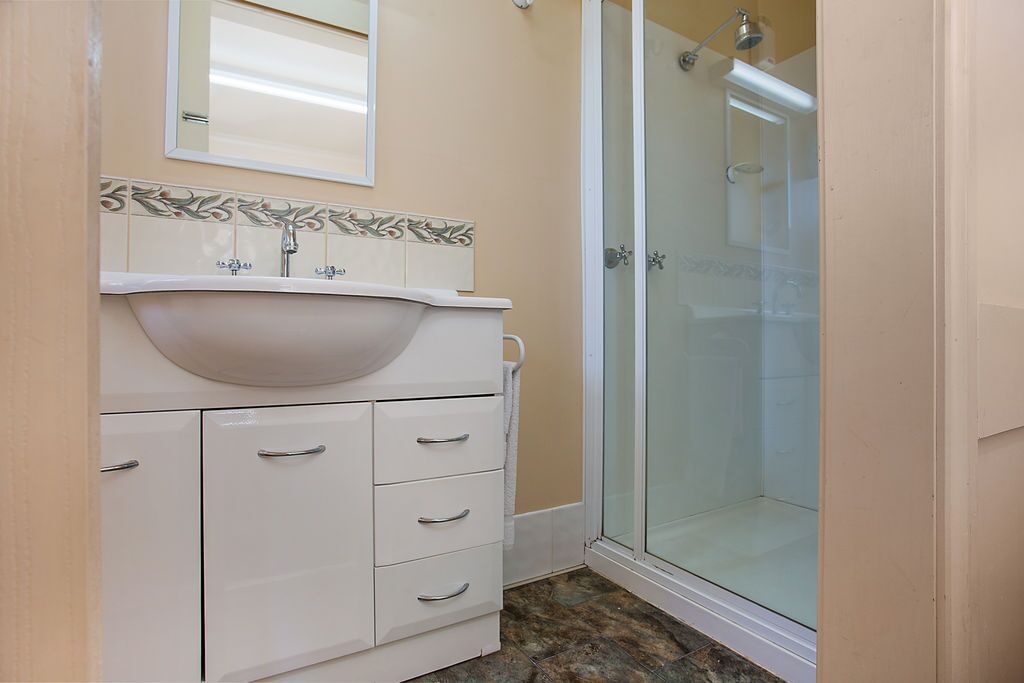 A bathroom with a white vanity, a mirror, a shower with a glass door, and patterned tiles on the wall.