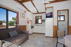 A compact living space with a sofa, a dining table, a kitchen area, and a large window offering a view of the outdoors. - Hamilton Caravan Park (Hamilton)