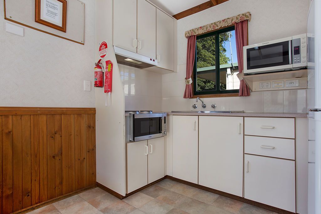 Una cocina compacta con gabinetes blancos, un microondas, una estufa y una ventana con cortinas.