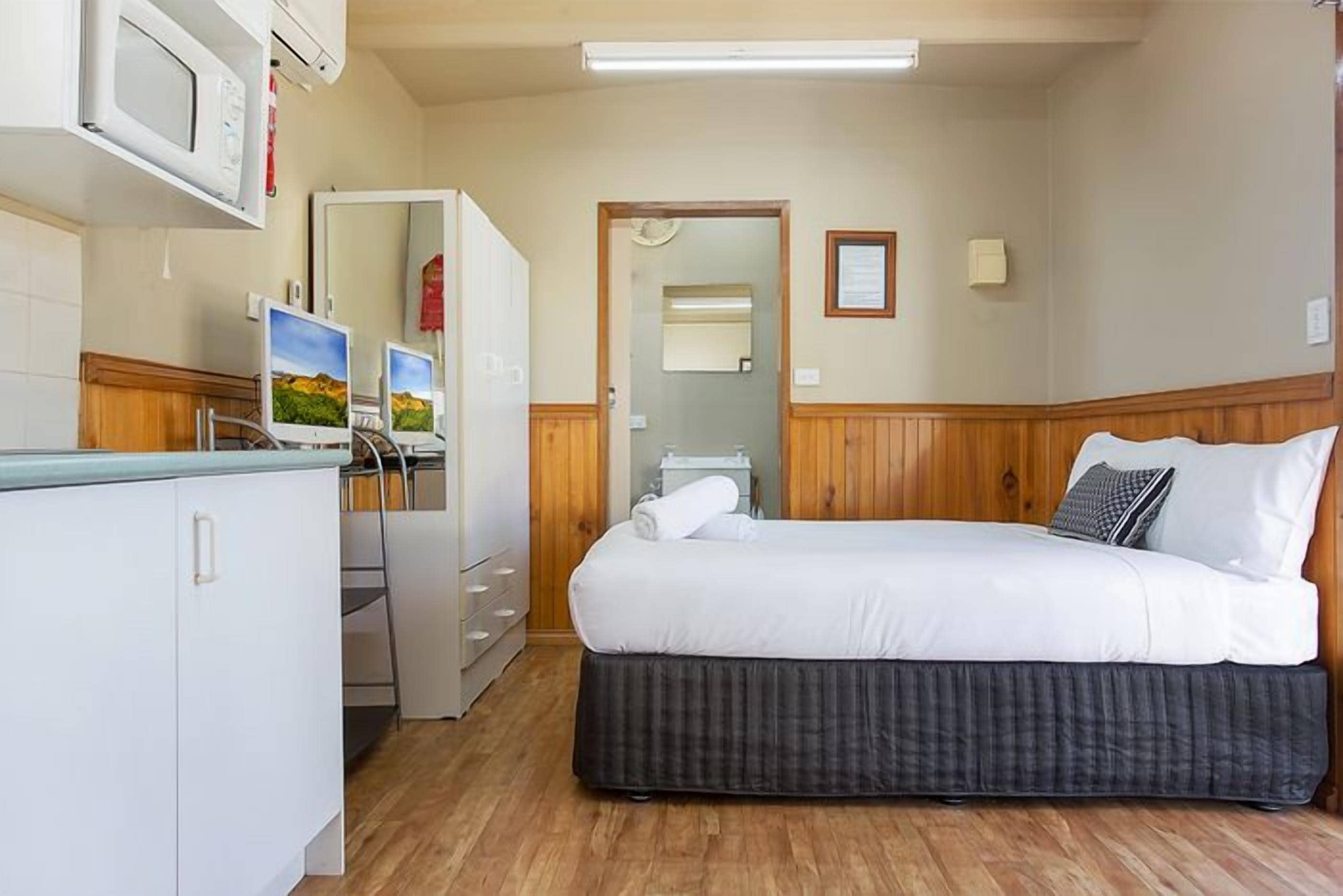 Una camera da letto con un letto, una scrivania con un computer, un forno a microonde e un armadio.
