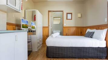 Una camera da letto con un letto, una scrivania con un computer, un forno a microonde e un armadio.