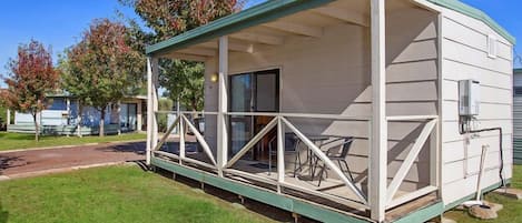 A single-story mobile home with a covered porch, a small patio area, and a visible door.
