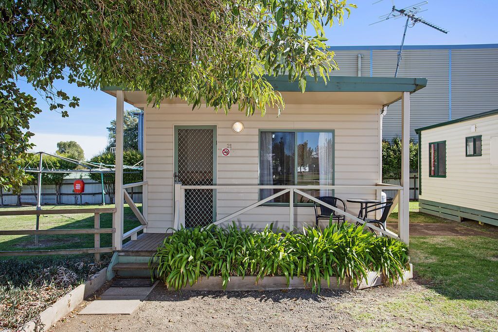 A small, single-story cabin with a porch, a small table and chairs, and a window.