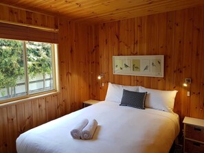A wooden-paneled bedroom with a bed, two bedside tables, a window, and a wall-mounted picture of birds. - Hamilton Caravan Park (Hamilton)