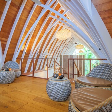 A high-ceilinged room with wooden beams, round seating with cushions, and a hanging light fixture.