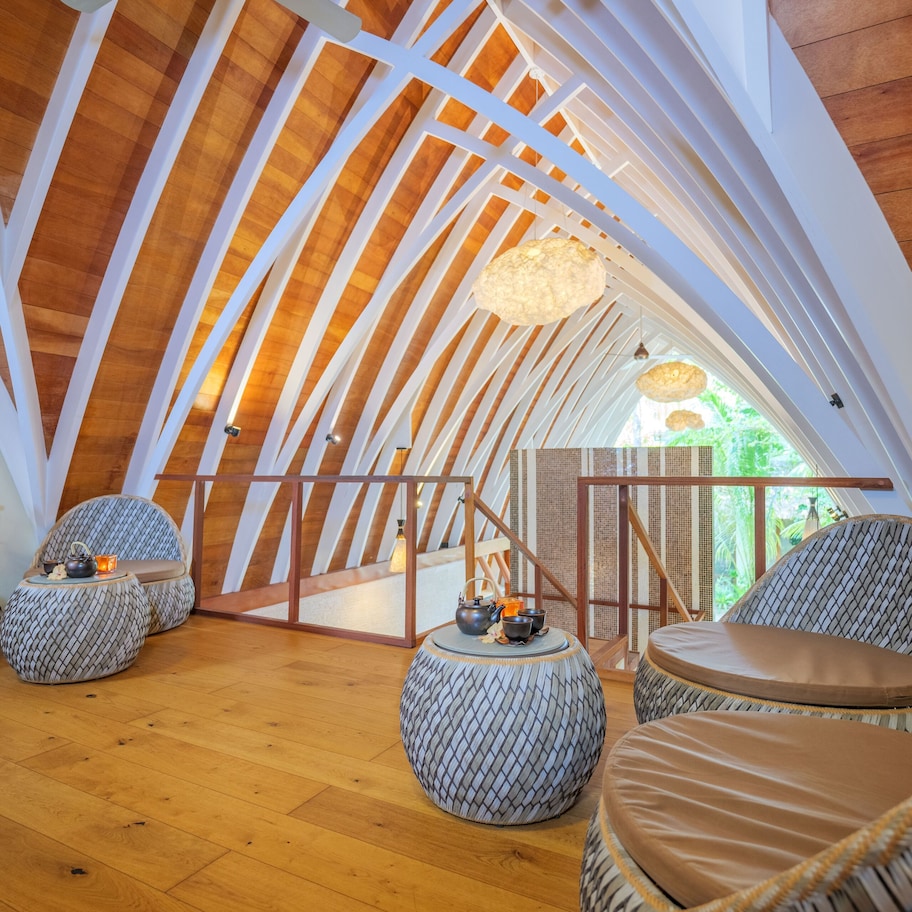 A high-ceilinged room with wooden beams, round seating with cushions, and a hanging light fixture.