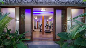 A gym with exercise equipment, a mirrored wall, and a thatched roof entrance.