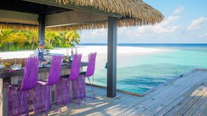 A wooden deck with a thatched roof bar area overlooking a beach.