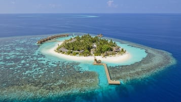 An aerial view of a tropical island resort with overwater bungalows, a white sandy beach, and clear turquoise waters.