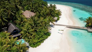 Vista aérea de un resort tropical con una playa de arena blanca, aguas turquesas cristalinas y exuberantes palmeras.