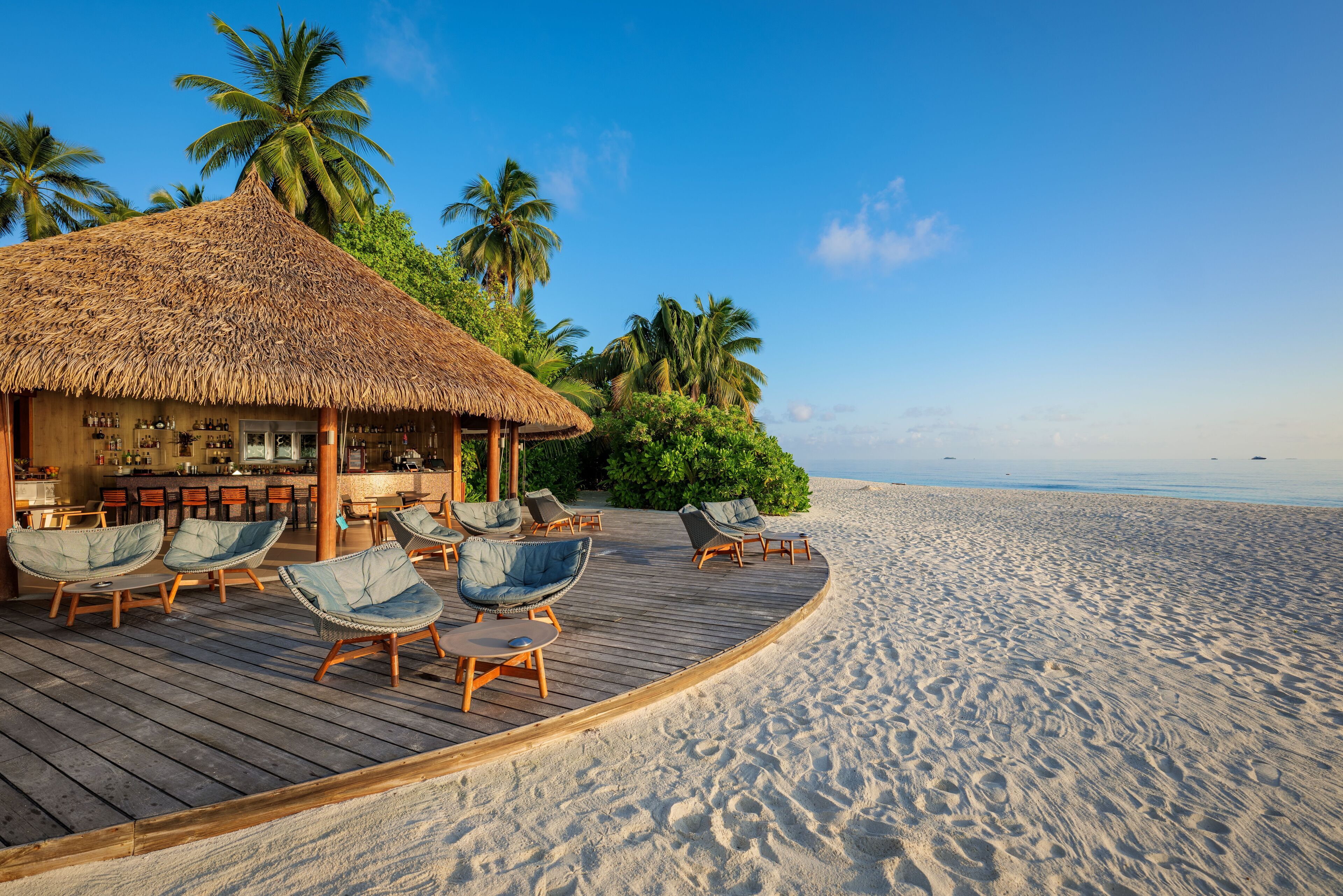 A beachside resort with a thatched-roof building, wooden deck, and lounge chairs.