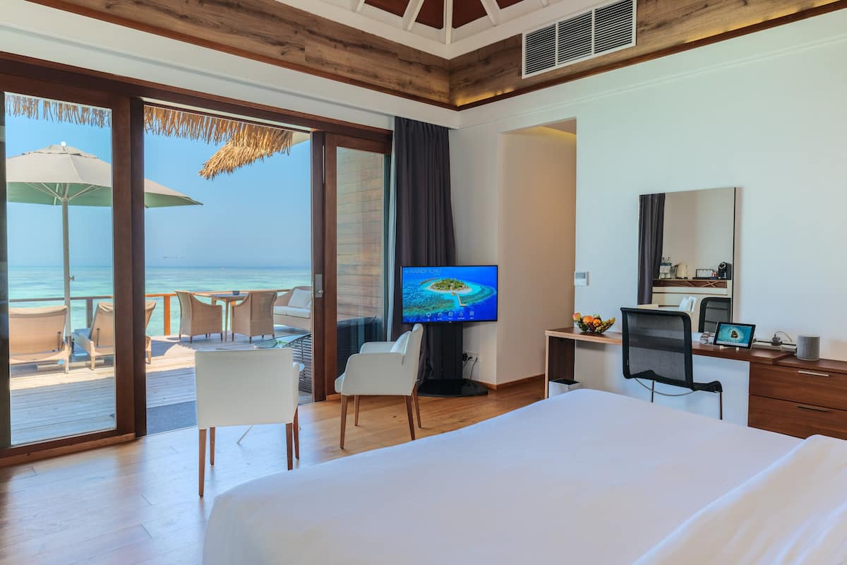 A hotel room with a large bed, a desk with a computer, a television, and a view of the ocean through large windows.