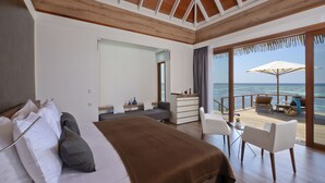 A bedroom with a large bed, a desk, and a view of the ocean through a sliding glass door.