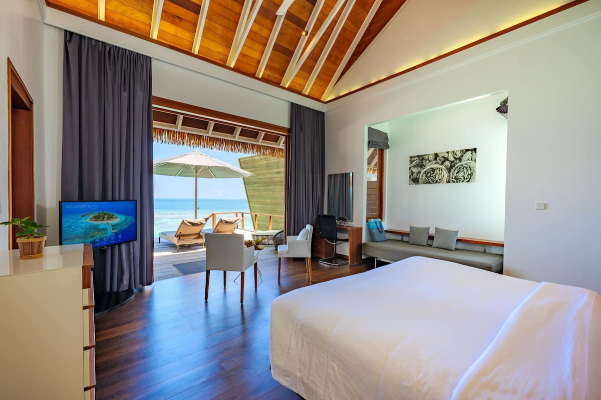 A modern hotel room with a large bed, a desk with a chair, a TV, and a view of the ocean.