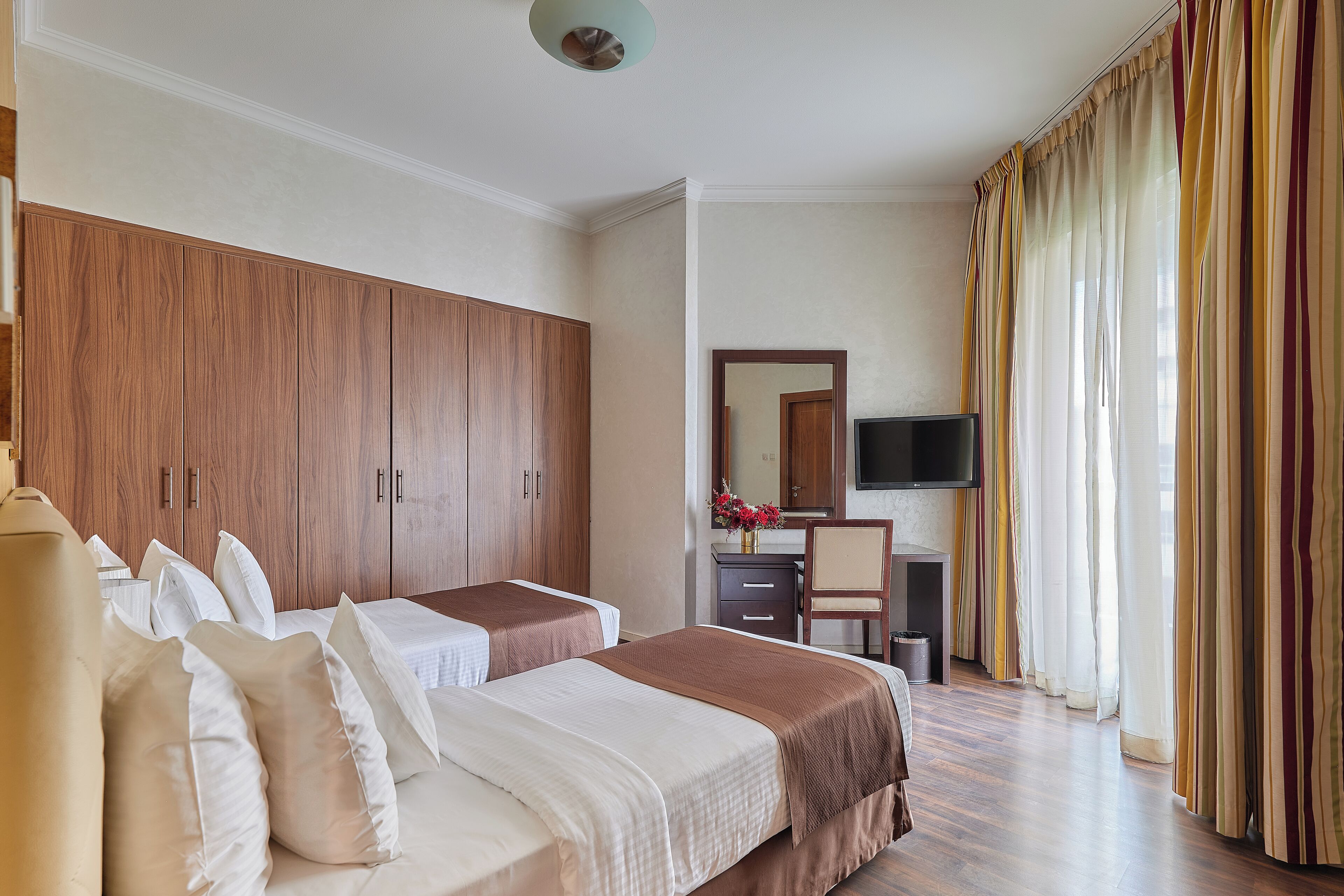 A hotel room with two beds, a wardrobe, a desk, a chair, and a television.