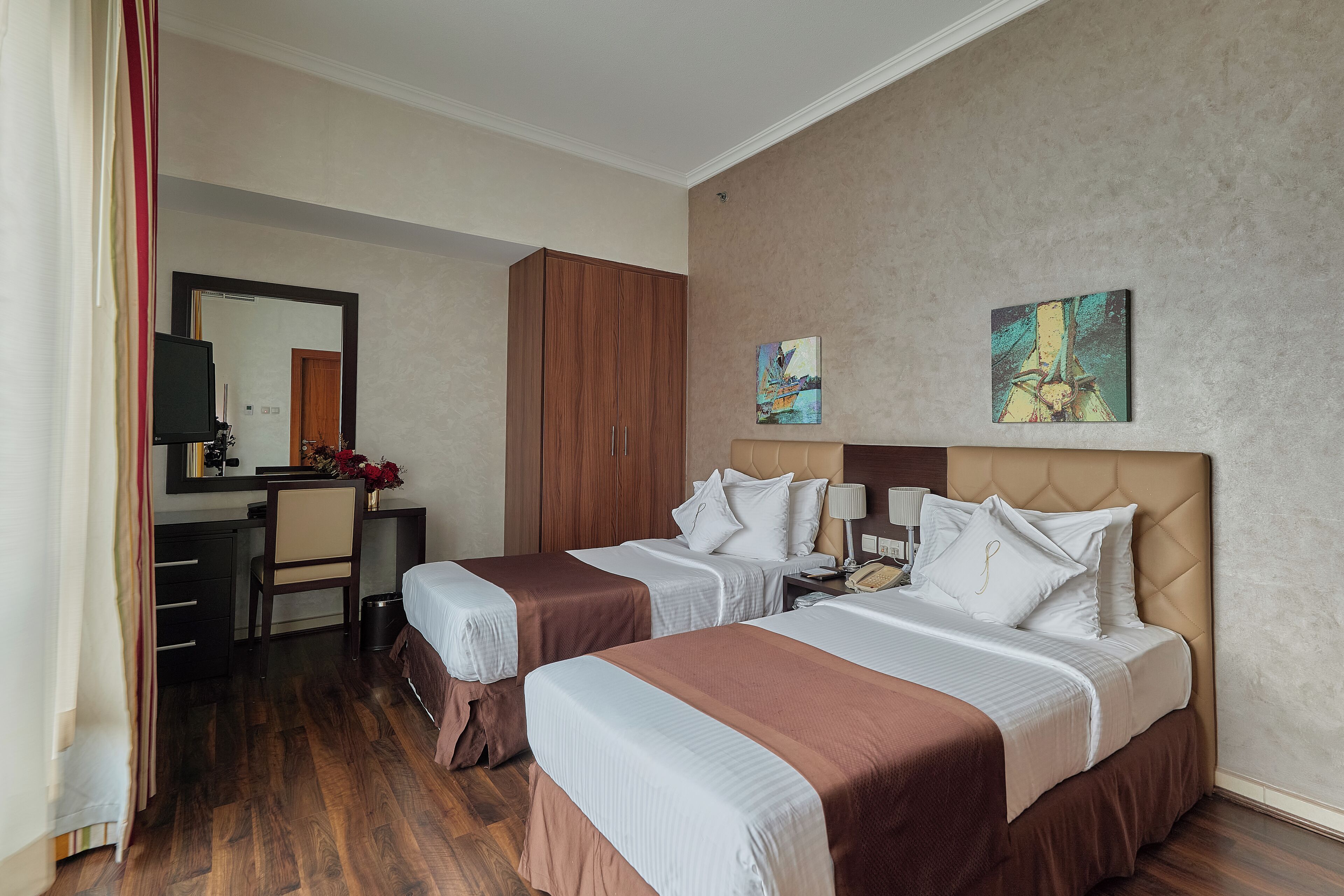 A hotel room with two beds, a desk, a mirror, and artwork on the wall.