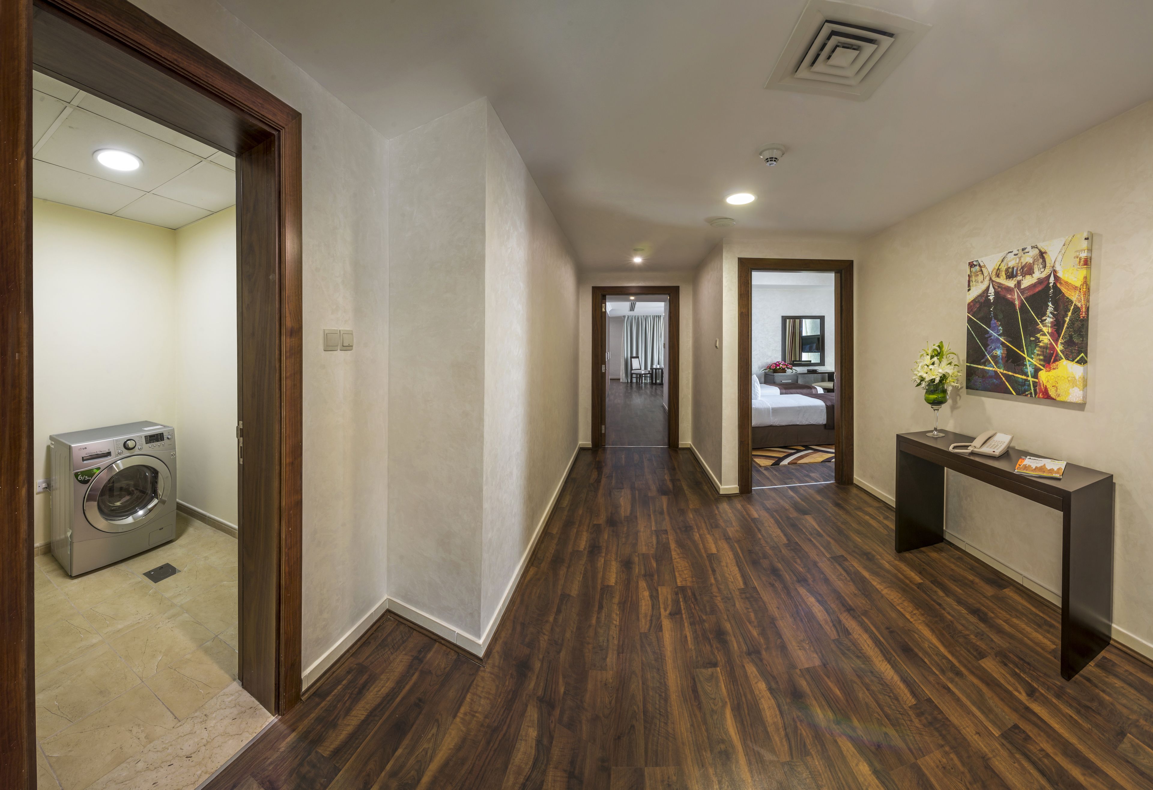 A hallway with a washing machine, a console table with a phone and a vase, and a painting on the wall.