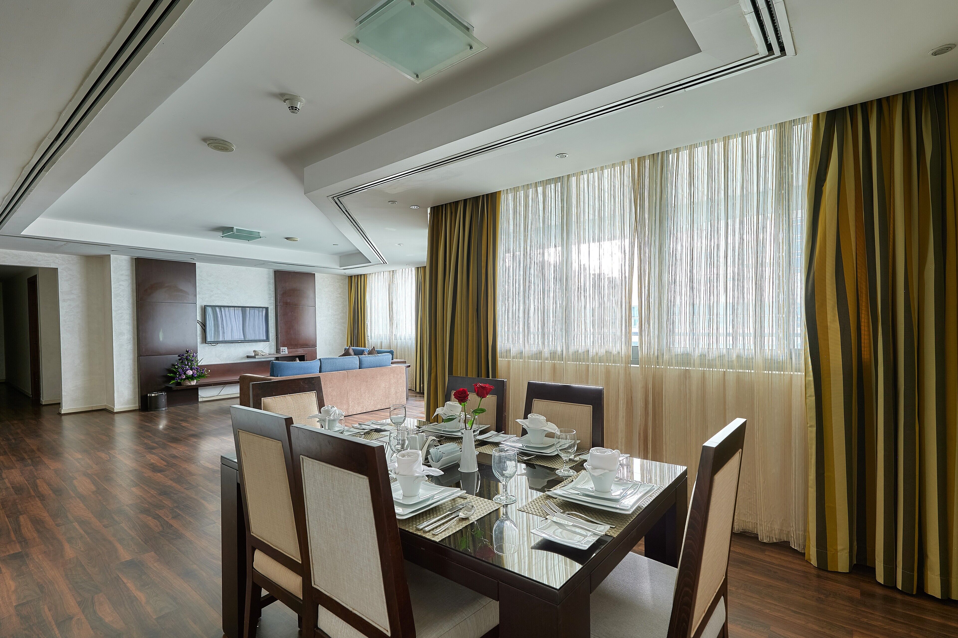 A dining area with a glass table set for six, surrounded by wooden chairs.