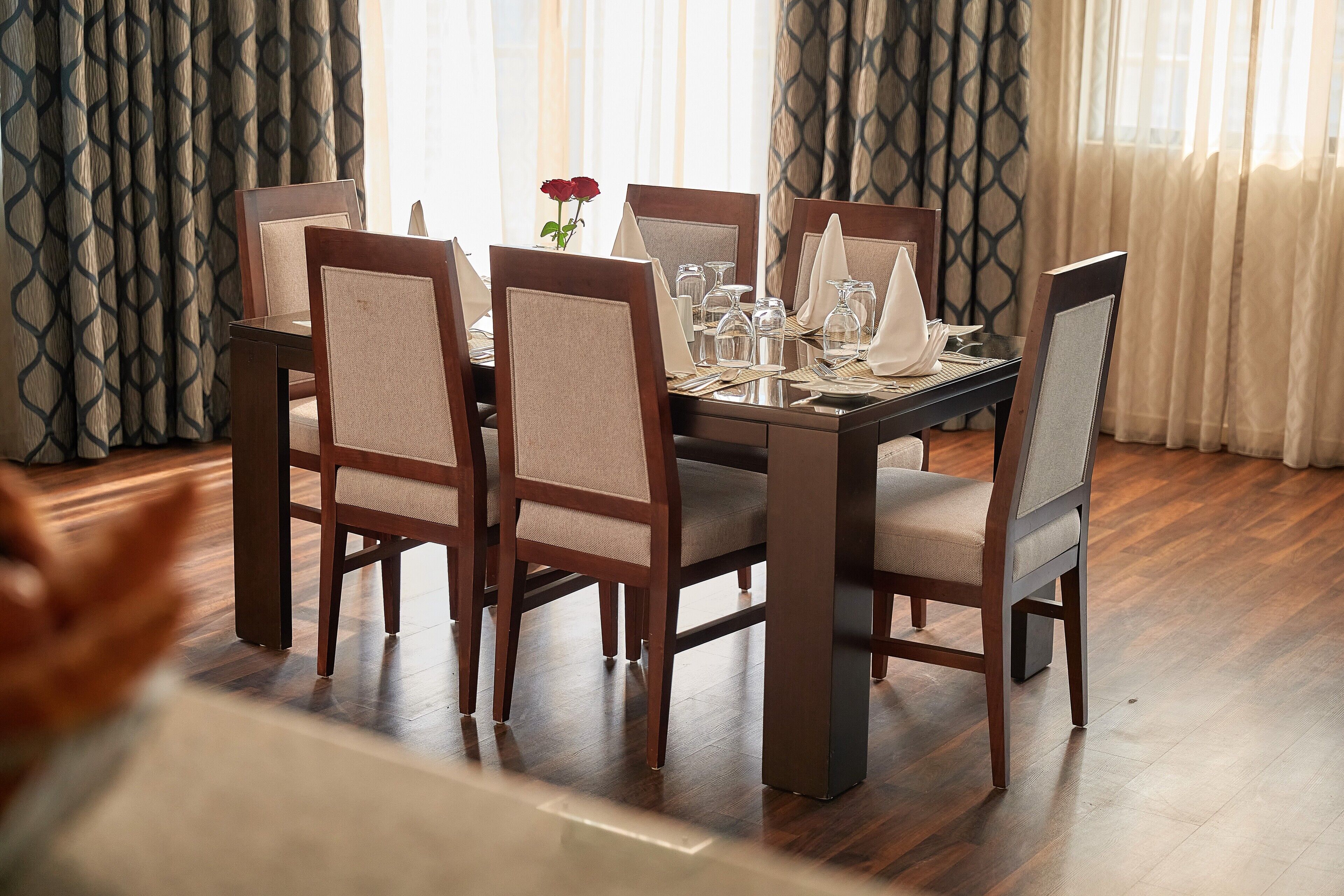 Uma sala de jantar com uma mesa retangular posta para quatro pessoas, cercada por cadeiras estofadas com estrutura de madeira.