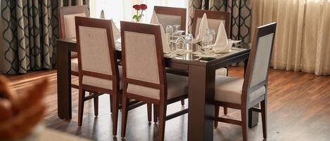 Uma sala de jantar com uma mesa retangular posta para quatro pessoas, cercada por cadeiras estofadas com estrutura de madeira.