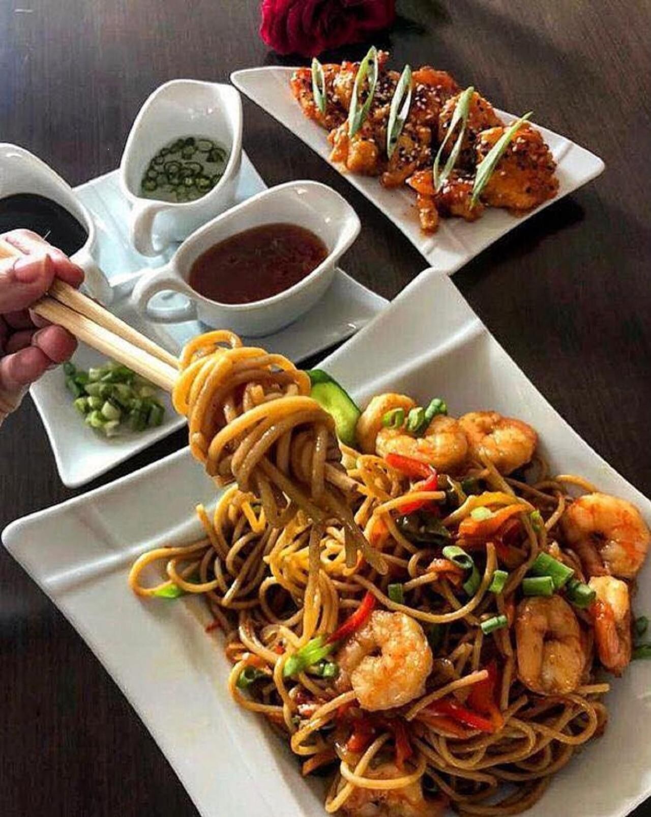 A plate of stir-fried noodles with shrimp and vegetables, a bowl of dipping sauce, and a plate of sashimi.