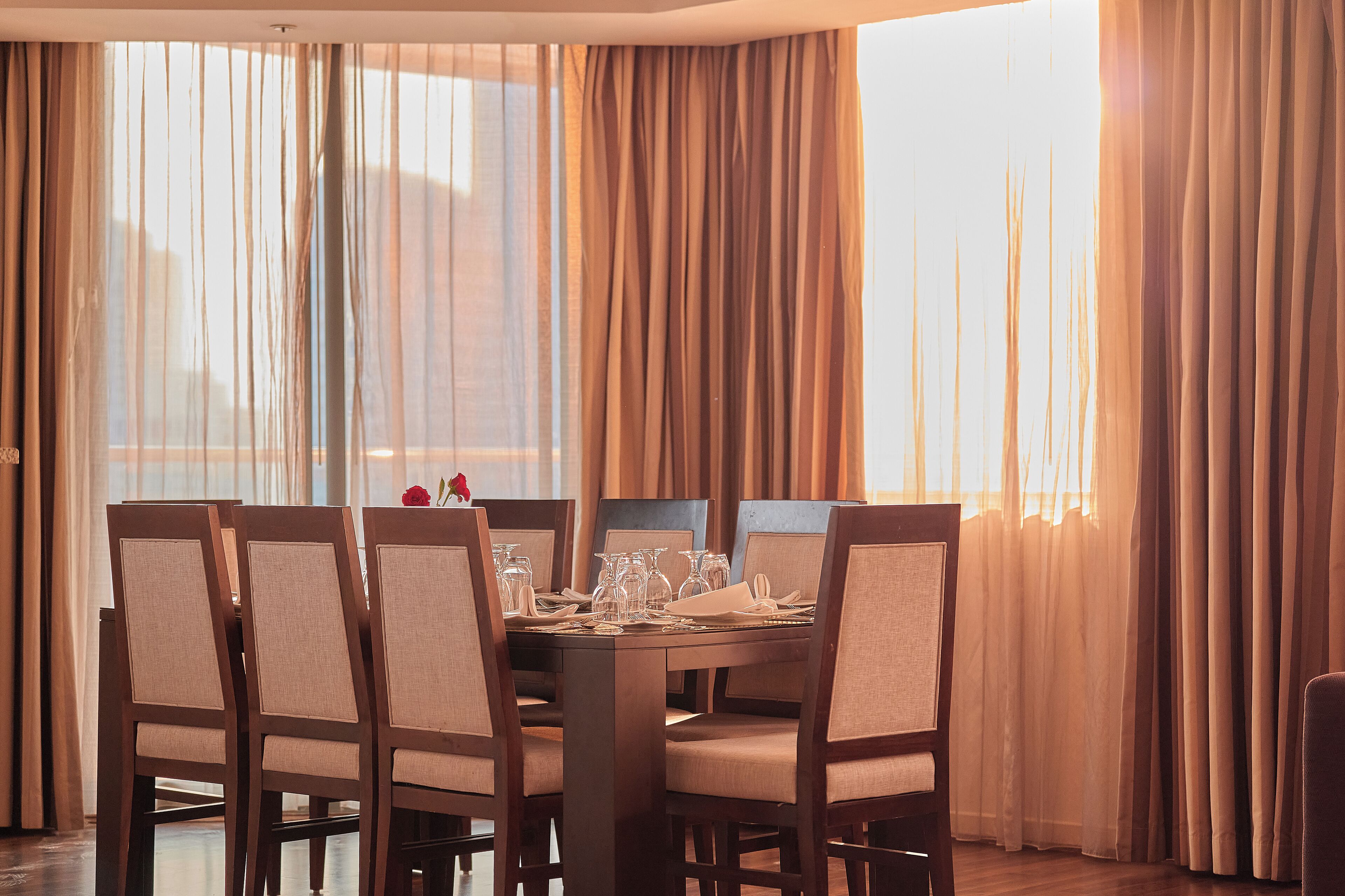 Uma sala de jantar com uma mesa de madeira posta para quatro pessoas, cercada por cadeiras estofadas.
