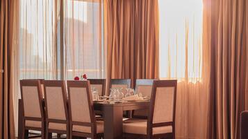 Uma sala de jantar com uma mesa de madeira posta para quatro pessoas, cercada por cadeiras estofadas.