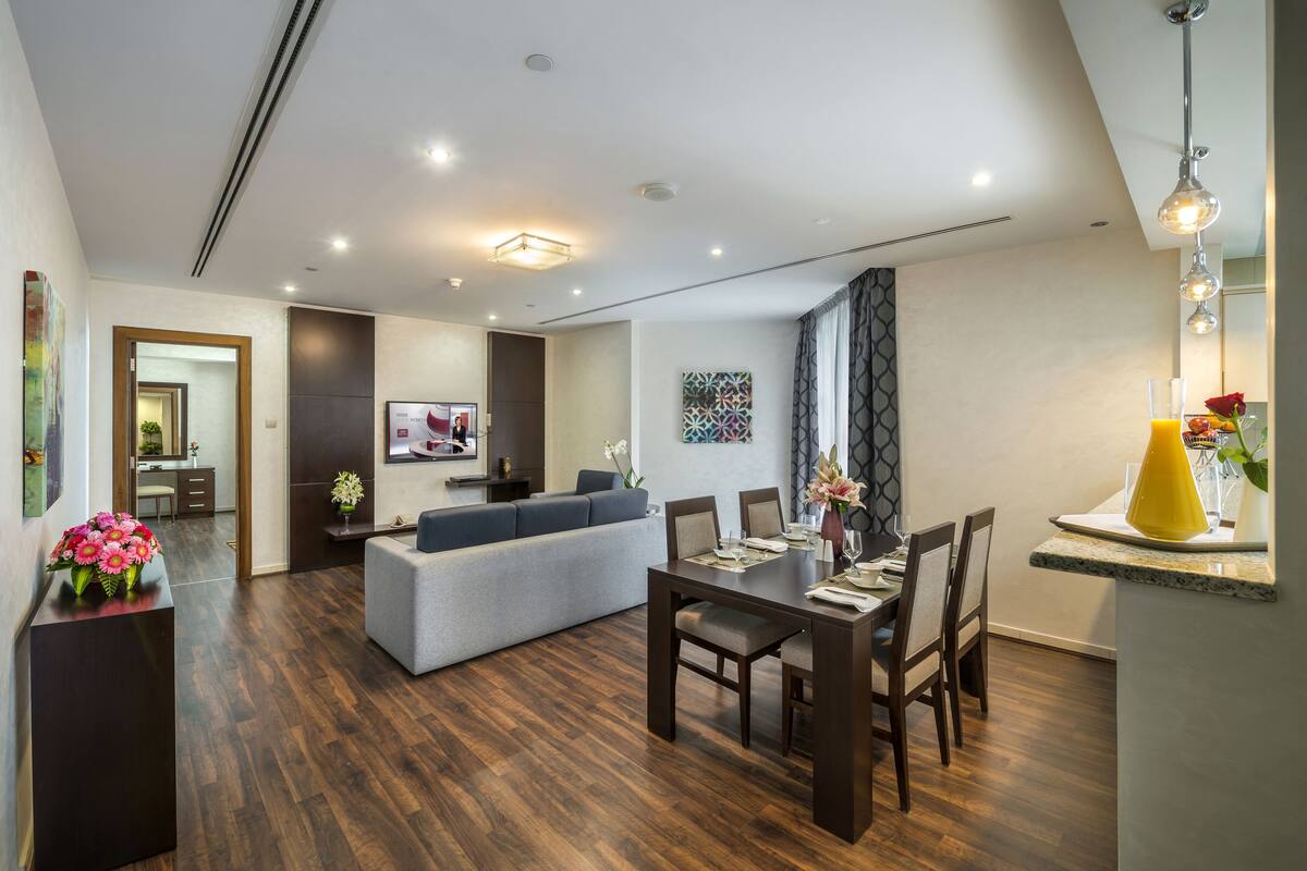 A modern living room with a dining area, wooden flooring, and a grey sofa.
