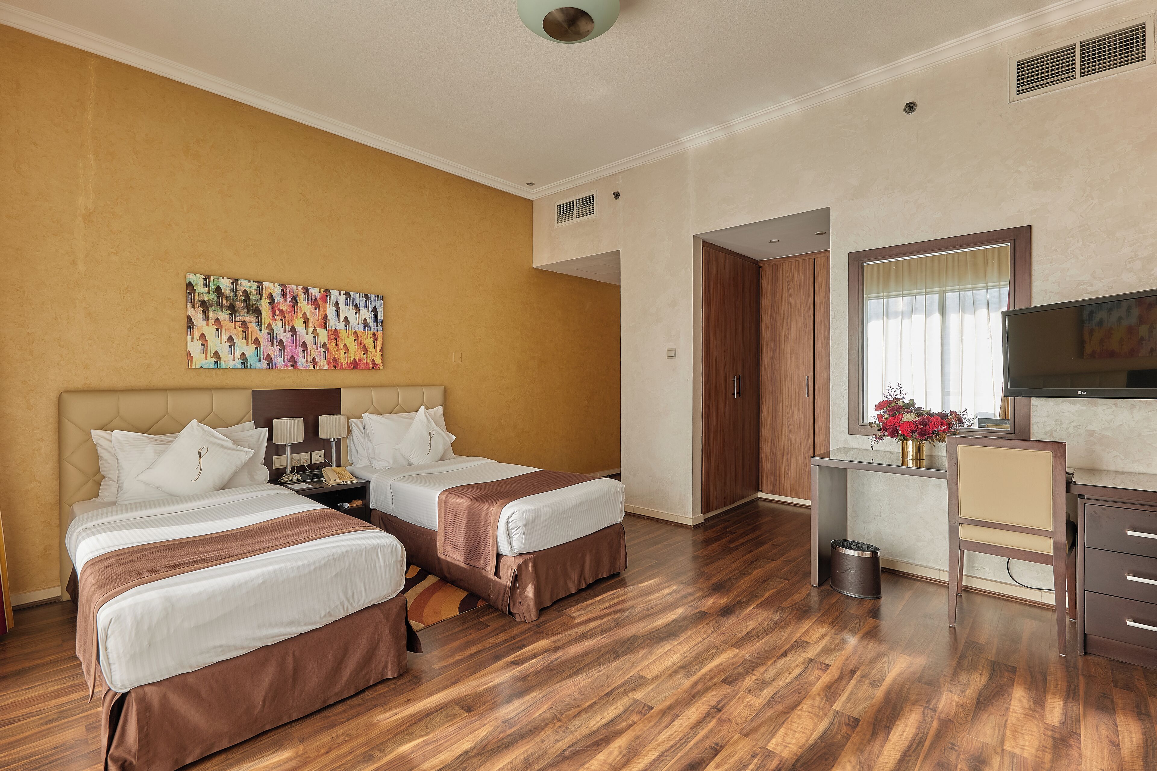 A hotel room with two beds, a desk, a TV, and a painting on the wall.