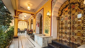 A grand entrance with ornate doors, a marble floor, and a seating area with tables and chairs. - Umaid Residency - A Regal Heritage Home (Amer)