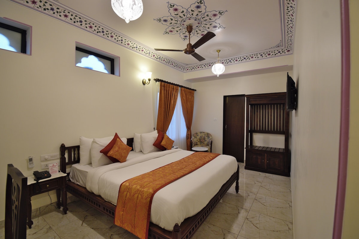 A bedroom with a large bed, a ceiling fan, a nightstand, a chair, and a door.
