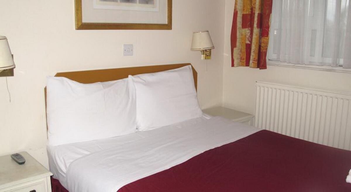Une chambre d’hôtel avec un lit, deux lampes de chevet, une fenêtre avec des rideaux et un radiateur.